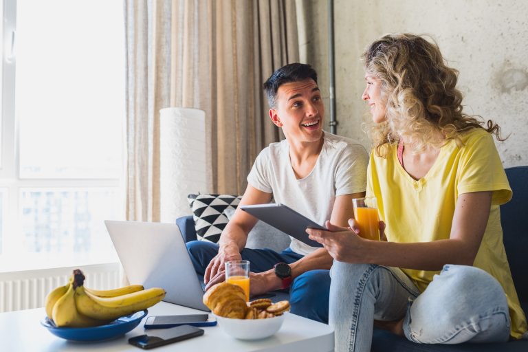 young couple sitting sofa home working online laptop tablet